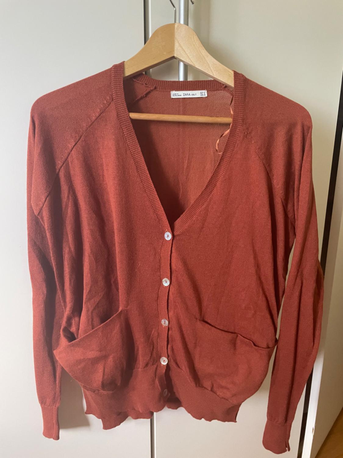 Front view of red cardigan with white buttons and front pockets.