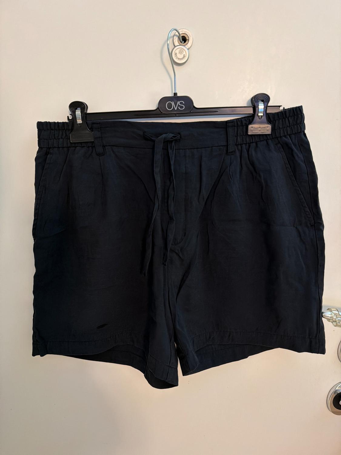Casual black shorts with an elasticated waistband and drawstring, hanging on a hanger with the text OVS on a white door.