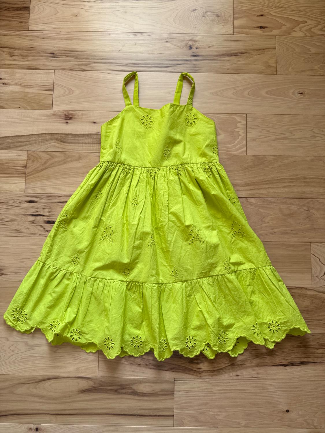 Yellow dress with thin straps, floral embroidery on the chest and skirt, on a light wood floor.