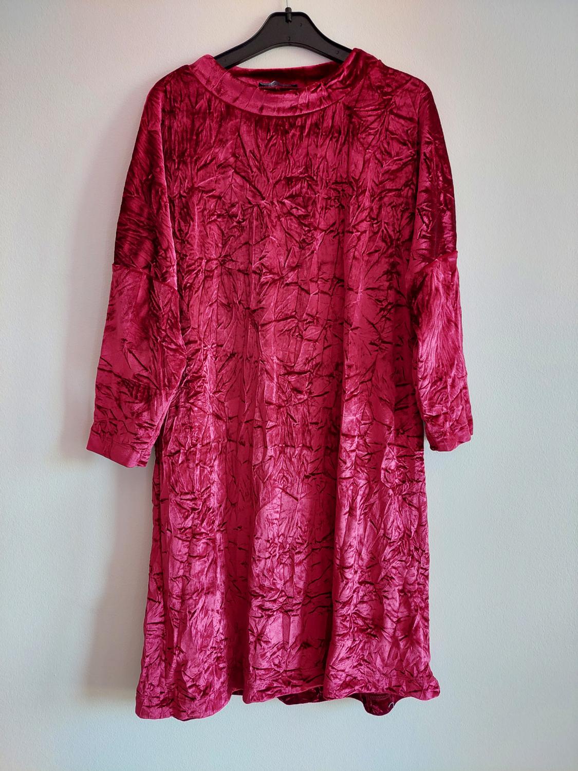 Dark fuchsia long-sleeved crushed velvet dress, hanging on a black hanger against a white wall.