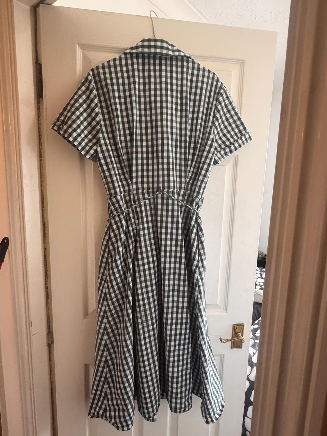 Green-and-white checked dress with short sleeves, a collar and a belt, hanging on a partly open white door to a room.