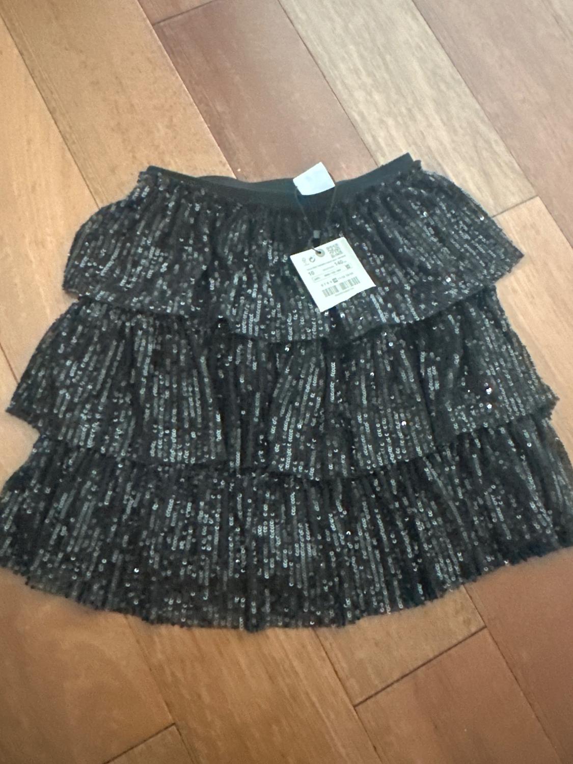 Black sequin skirt with ruffles on a wooden floor. Visible label with barcode and product details.