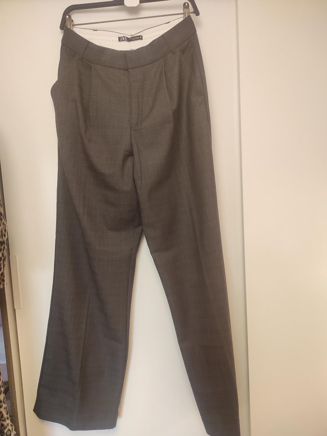 Front view of grey trousers with side pockets and a zip fastening.
