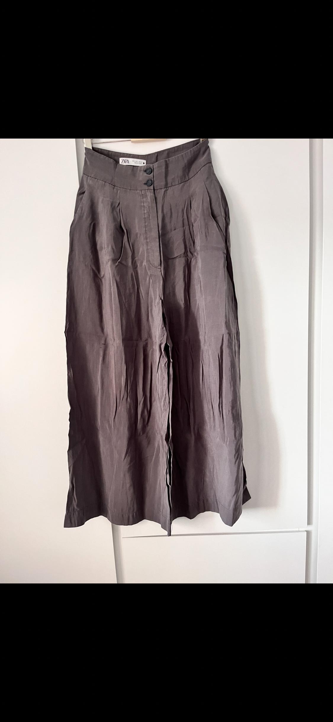 Long, grey, crinkled skirt hanging on a white hanger, with two buttons at the waist. Visible label with "ZARA" text.