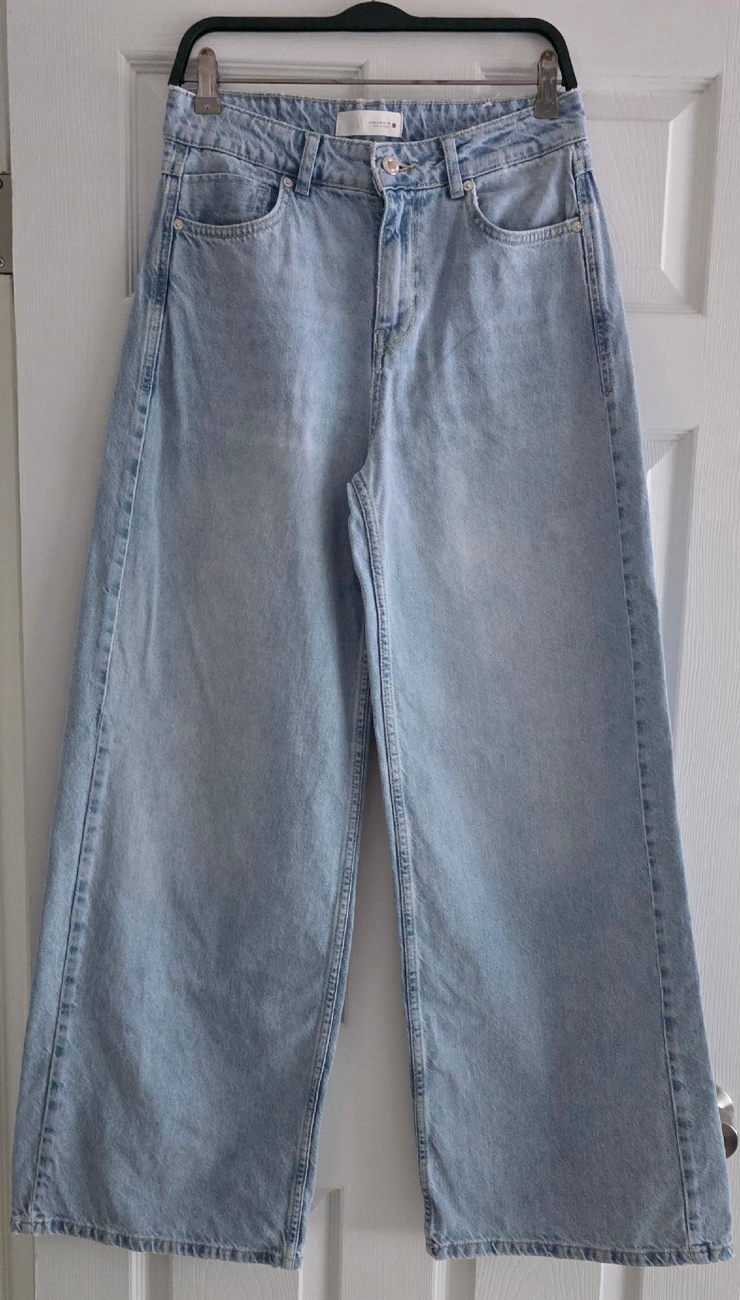 Light blue wide-leg jeans hanging on a black hanger over a white door.