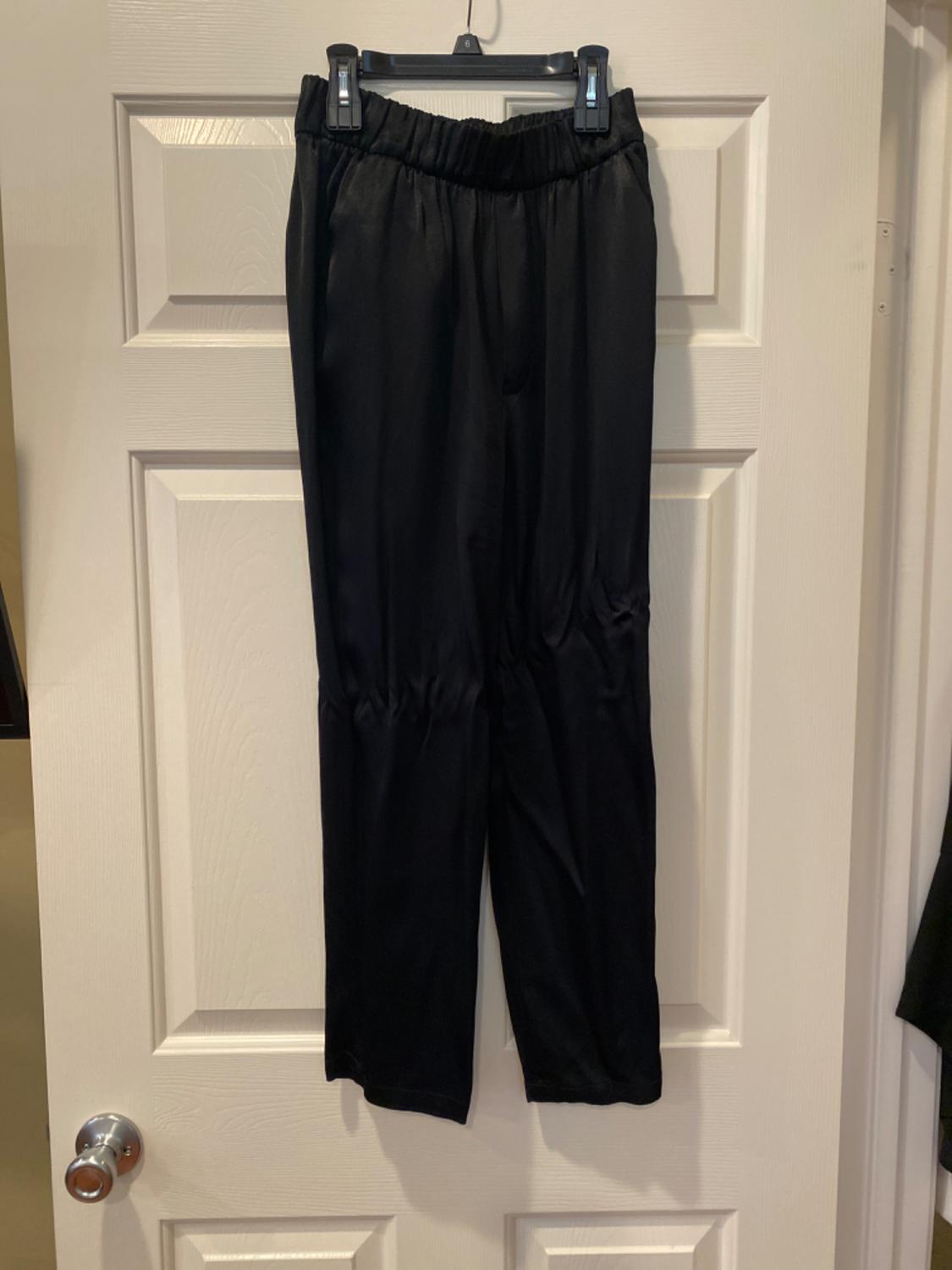 Black lightweight fabric trousers with an elasticated waistband, hanging on a hanger in front of a white door with a silver doorknob.