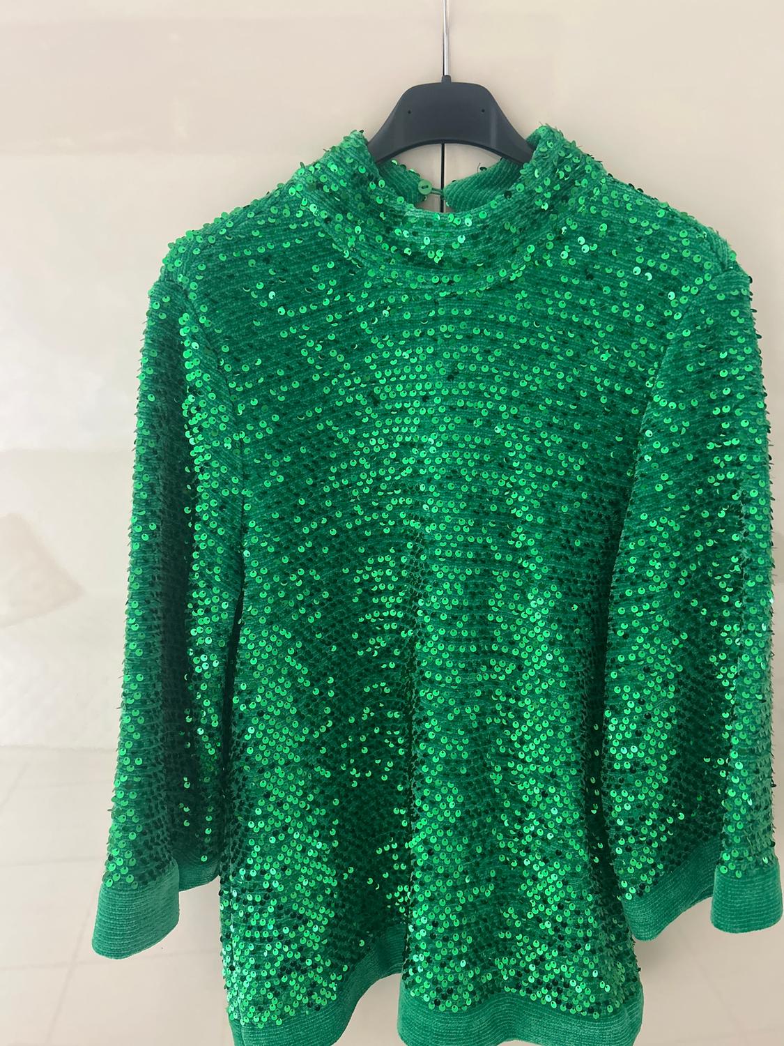 Bright green sequined jumper hanging on a black hanger against a light background.