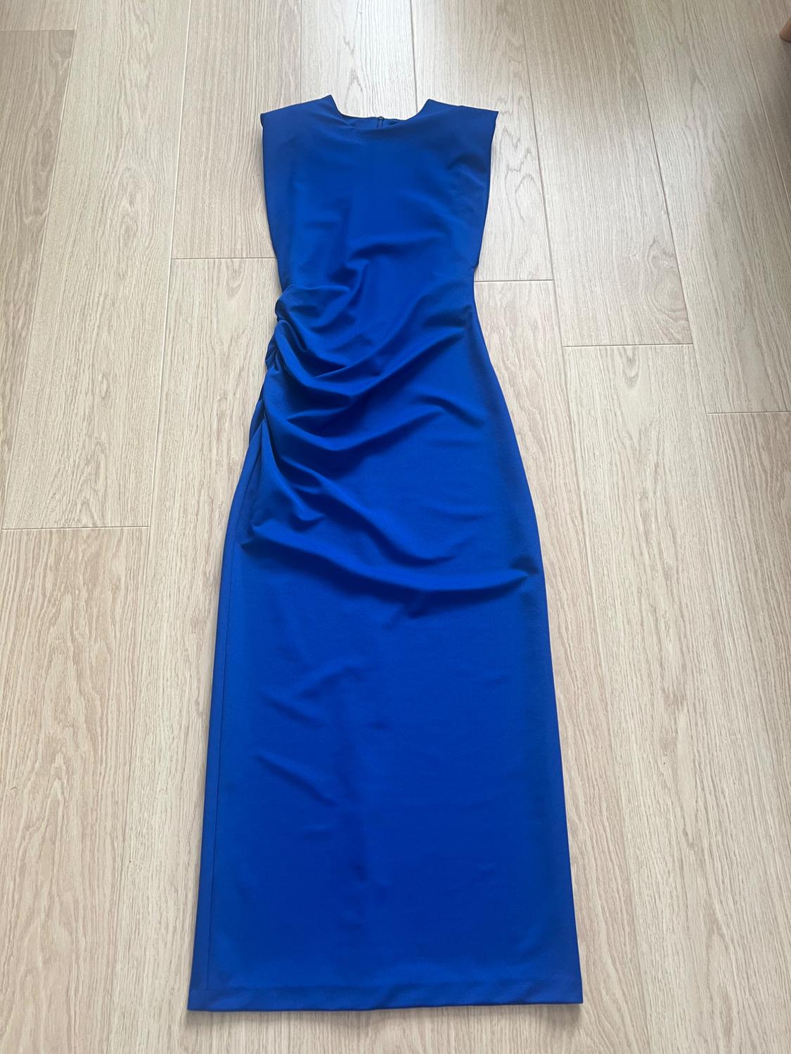 Blue sleeveless maxi dress with ruched detailing on the side, laid out on a light wood floor.