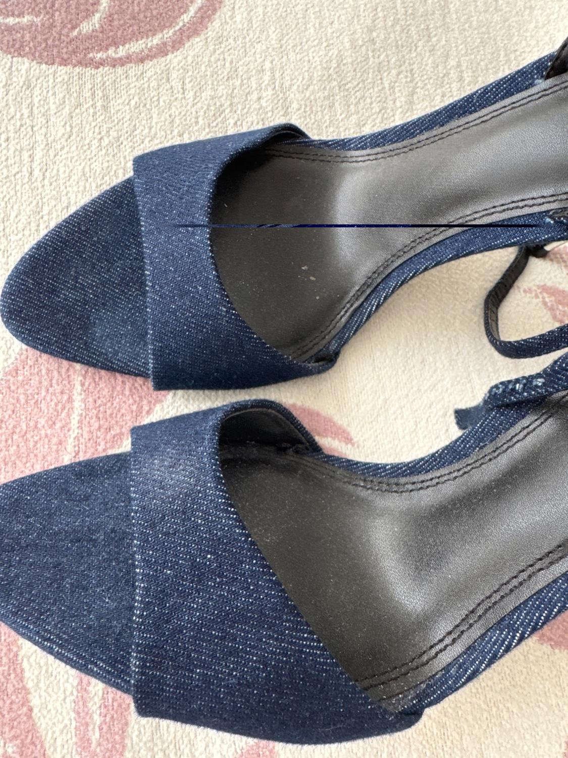 Dark blue high heels with an open-toe design on a light rug with pink accents.