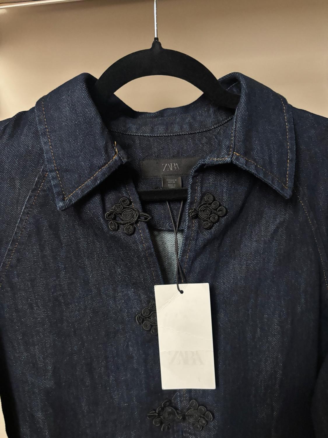 Dark blue denim shirt on a black hanger. Its collar, black decorative fastenings and white label stand out. Visible text: ZARA.