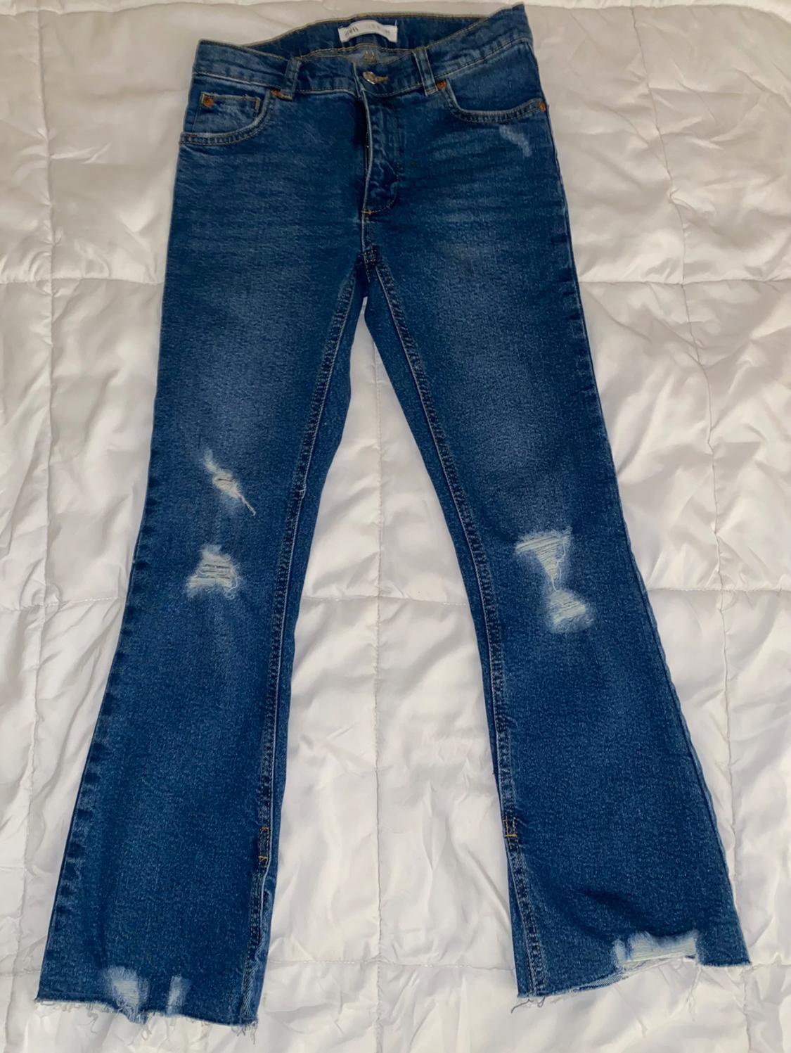 Front view of blue jeans with distressed details and frayed hems.