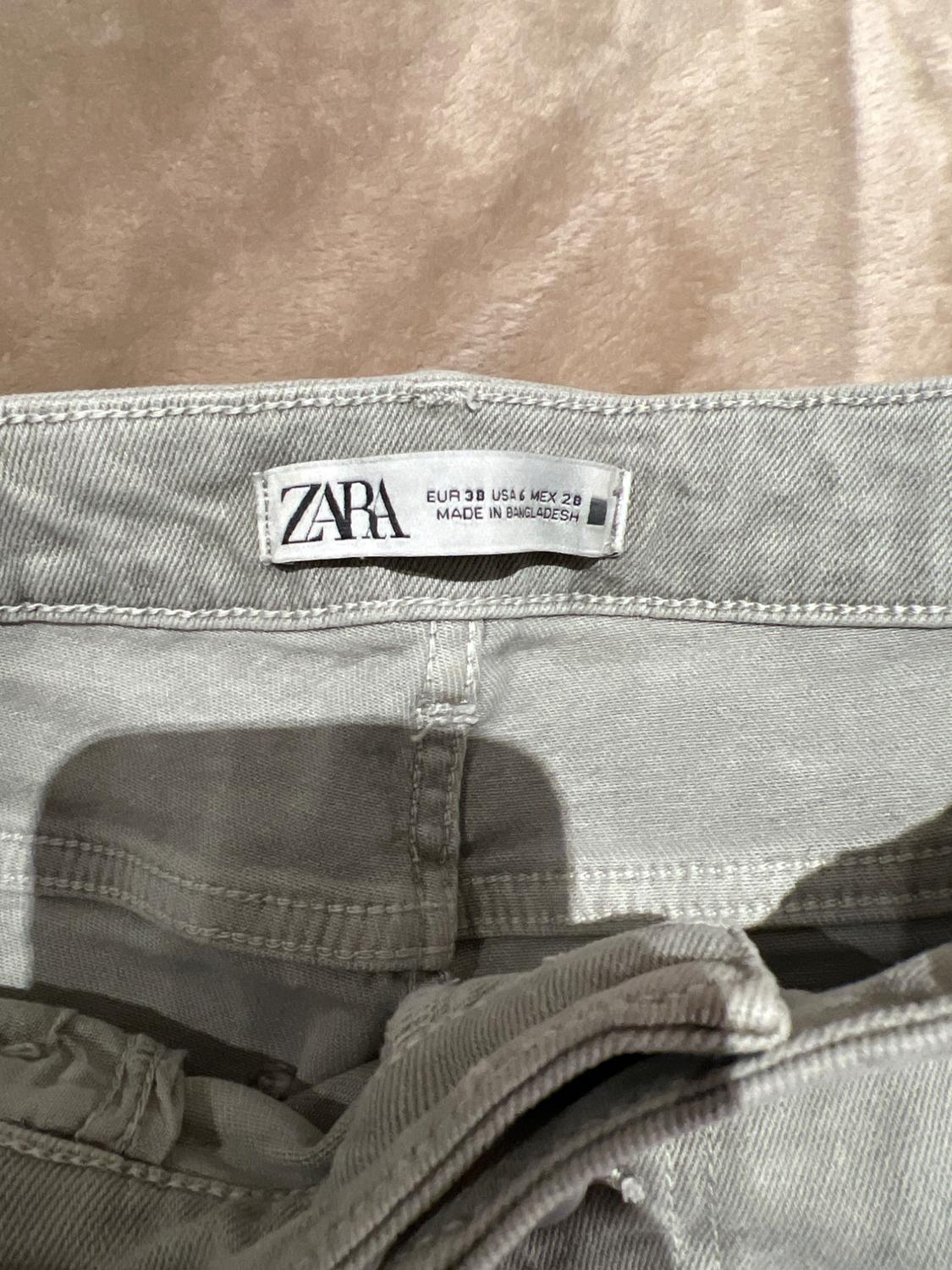 Grey trousers label with the brand ZARA, size EUR 38 USA 6 MEX 28, made in Bangladesh, on a beige background.