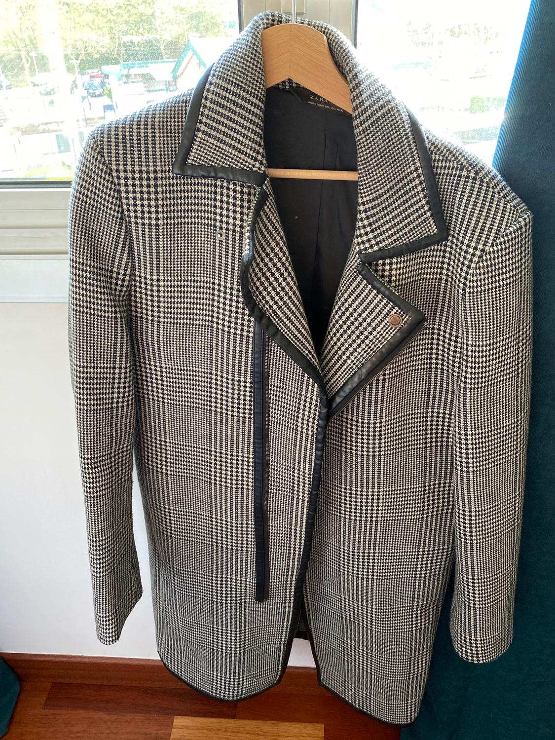 Front view of a checked coat with a black lapel and zip fastening, hanging on a hanger.
