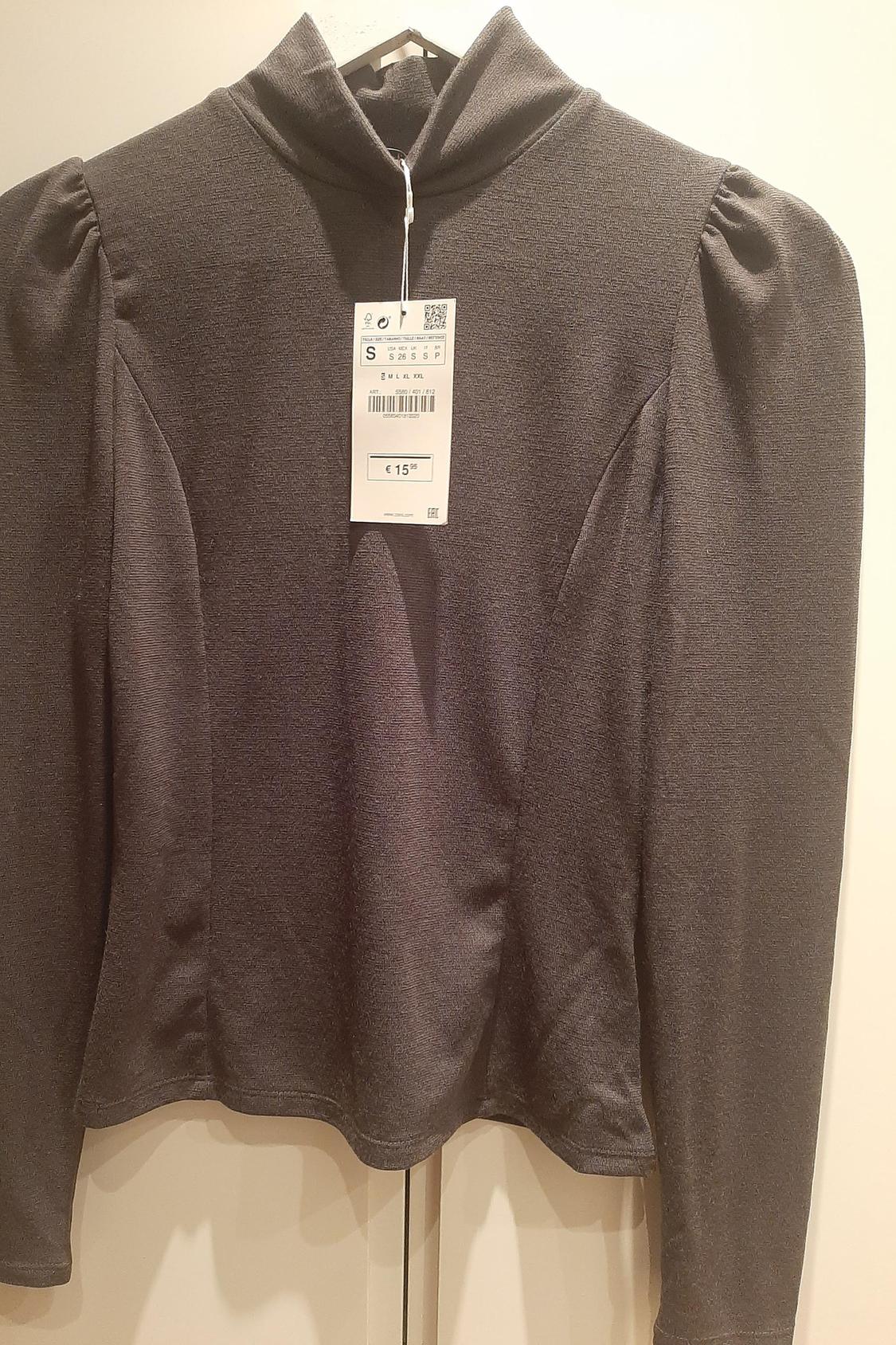Front view of a grey long-sleeved blouse with a roll neck and visible label.