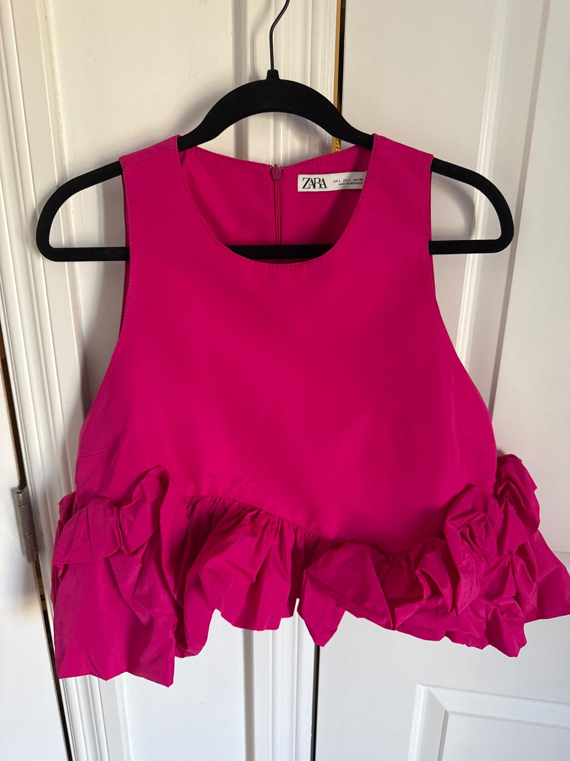 Fuchsia sleeveless top with frills on the hem, hanging on a black hanger. Visible label: "ZARA". White door background.