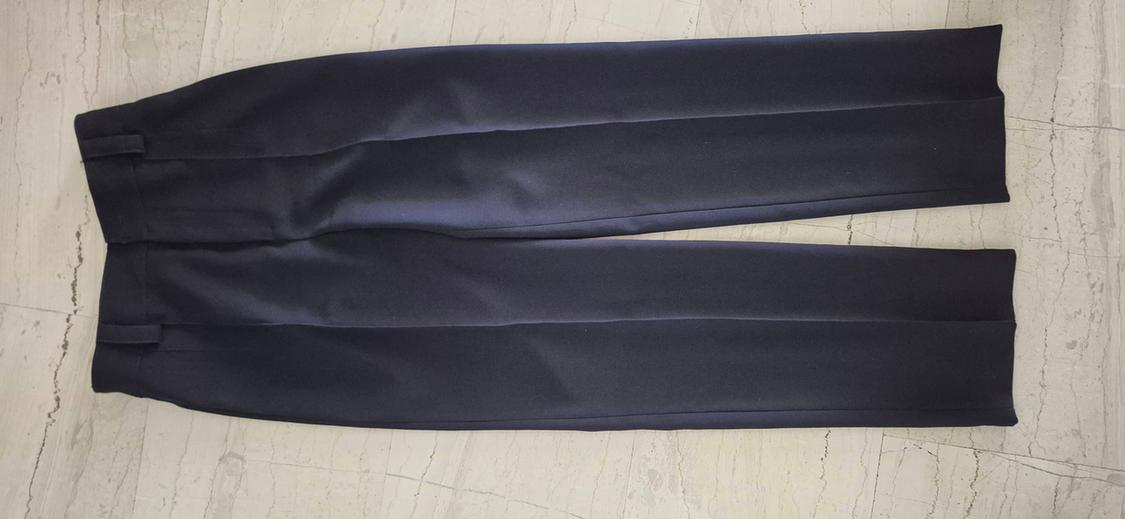 Black tailored trousers with pleats, laid on a light marble floor.