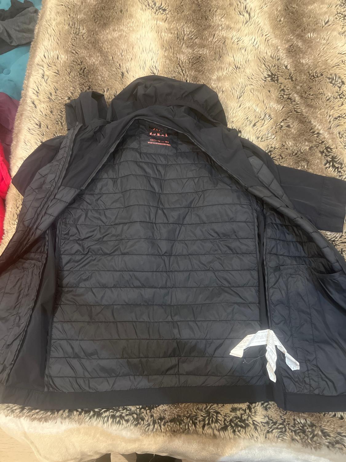 Open black jacket on a faux fur blanket. The internal label with red and white text is visible.