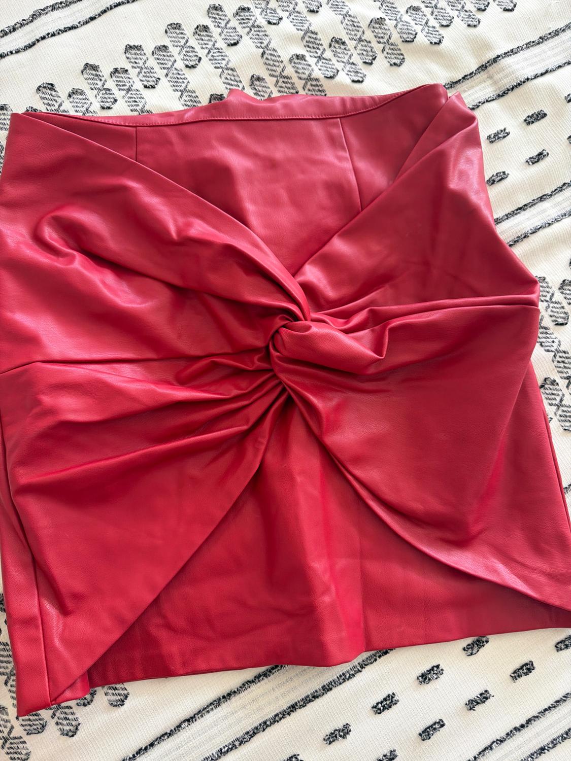 Red skirt with a front knot and pleats, on a white rug with texture and black geometric patterns.