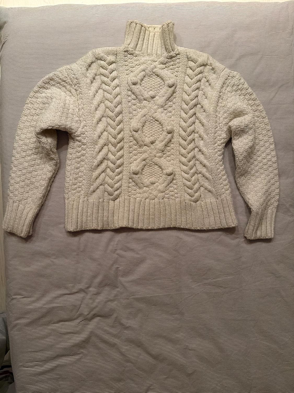 Chunky cream cable knit roll neck jumper, placed on a striped fabric surface.