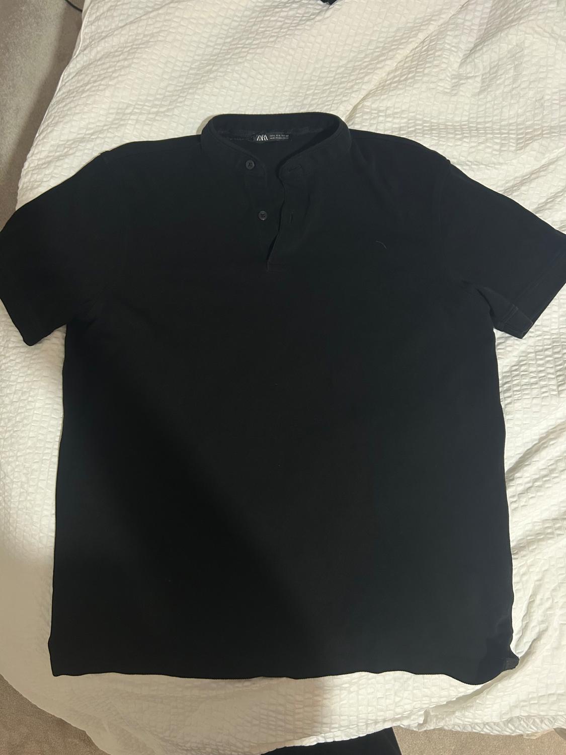 Black short-sleeved T-shirt with a grandad collar and buttons, placed on a textured white duvet.