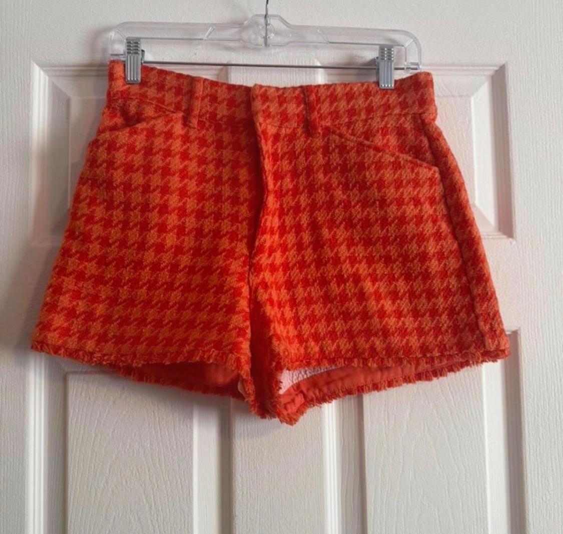 Red and orange checked fabric shorts, hanging on a clear hanger over a white door.