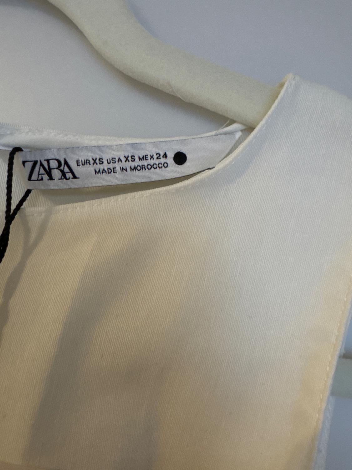 Label of a white Zara garment on a hanger, showing sizes EUR XS, USA XS, MEX 24, and "Made in Morocco."