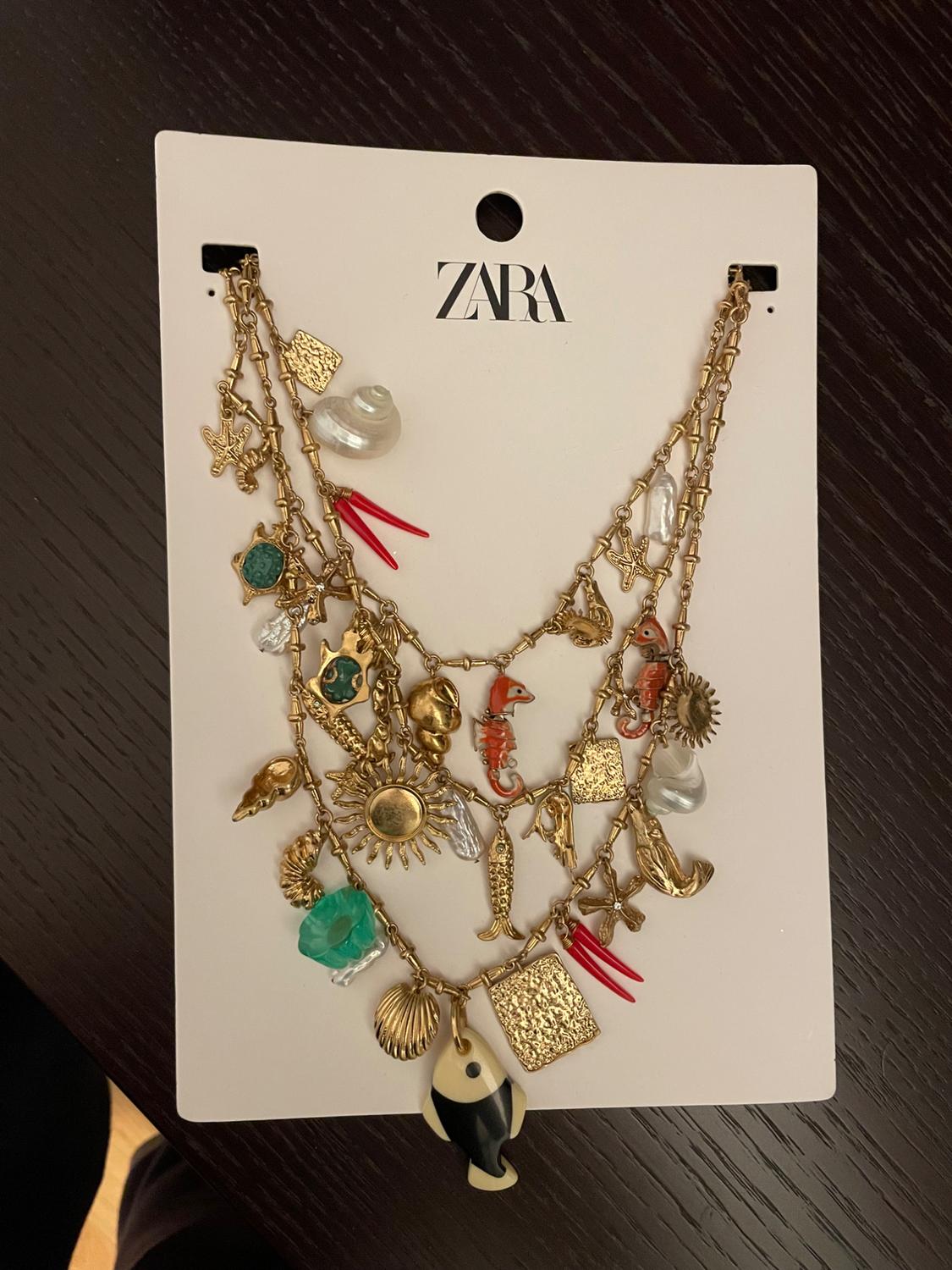 Zara necklace with gold sun, seahorse, shell, and stone pendants on a white card on a dark table.