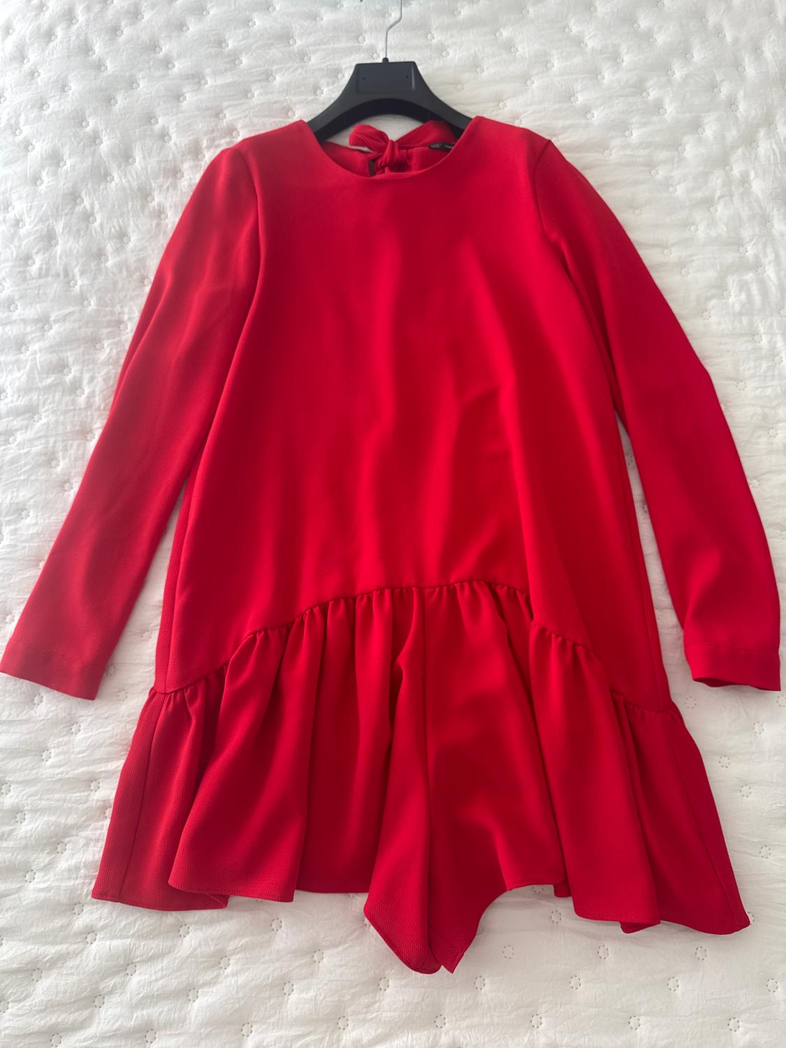 Long-sleeved red dress with ruffles on the bottom, hanging on a black hanger over a white quilted bedspread.