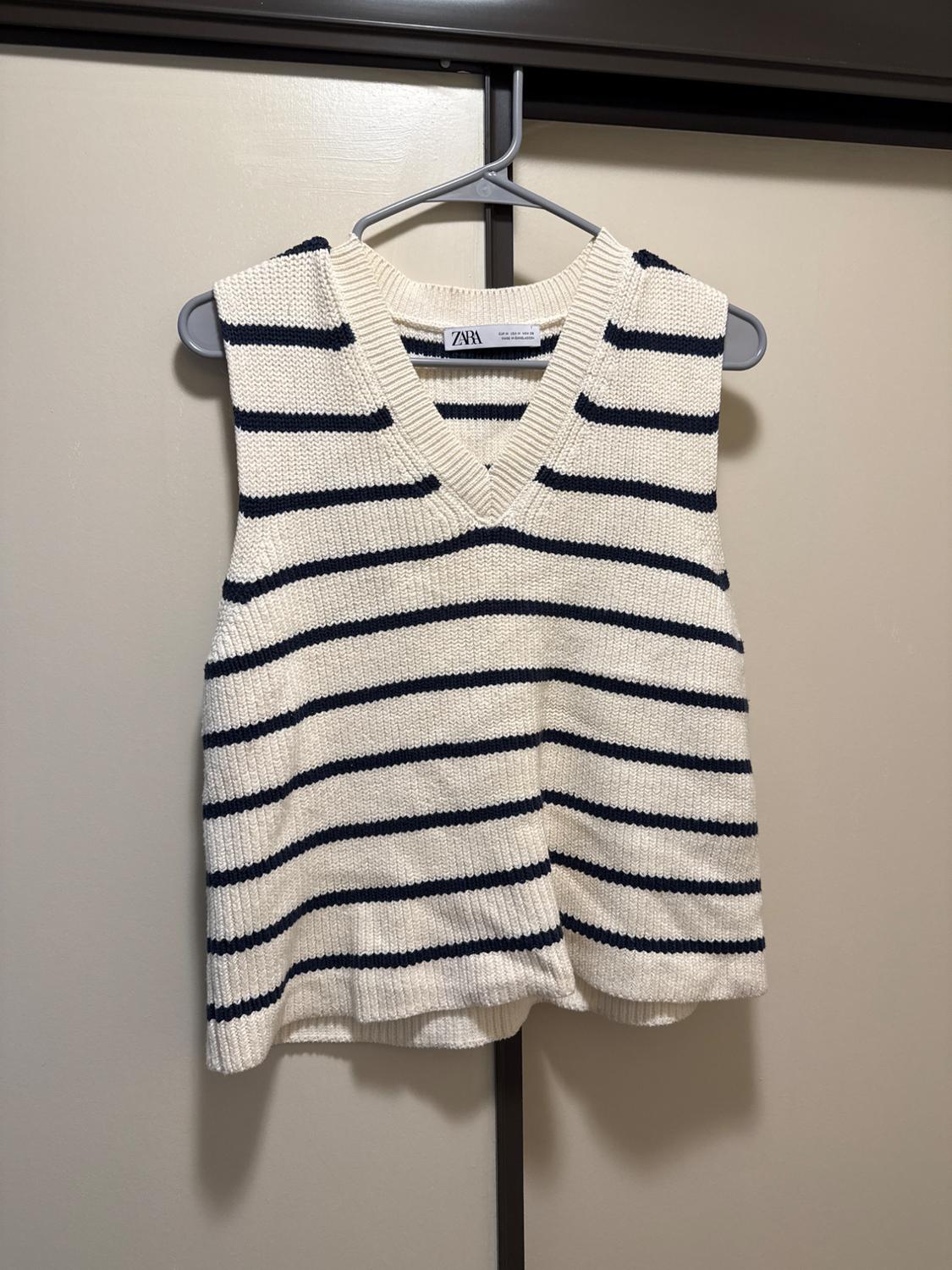 Knit vest with horizontal stripes and a V-neck, hanging on a hanger. ZARA label visible on the inside.