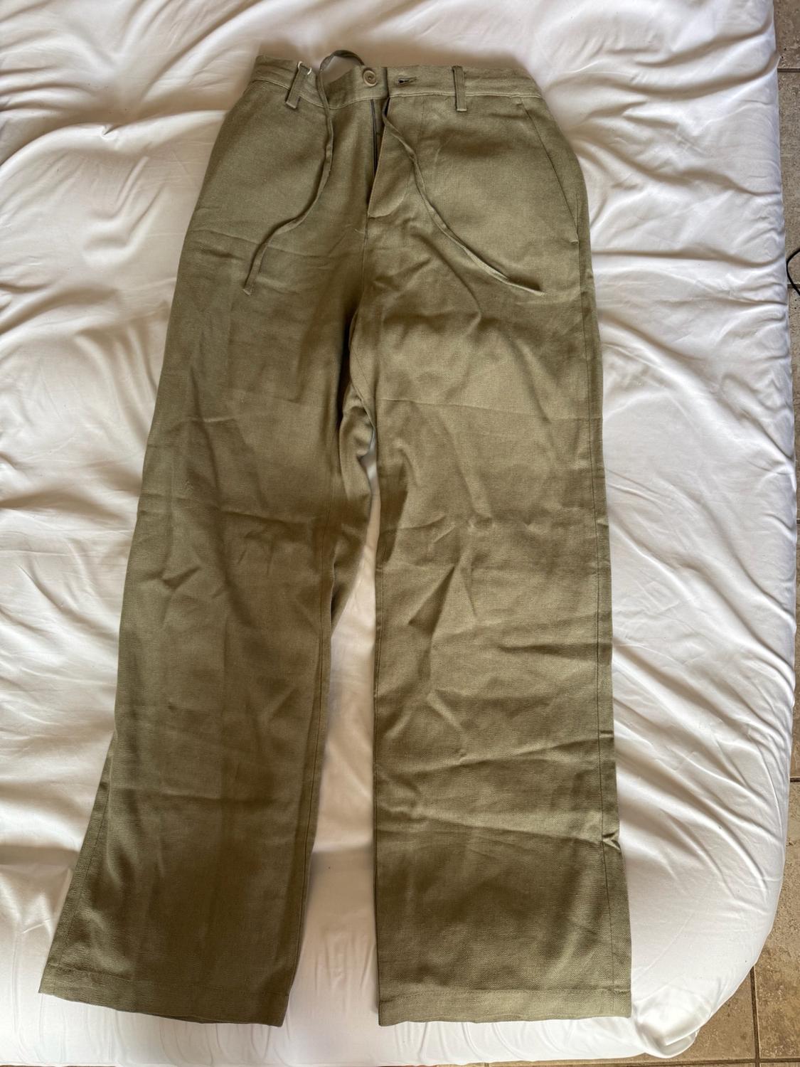 Olive-green trousers with a drawstring waist, laid out on crumpled white sheets.