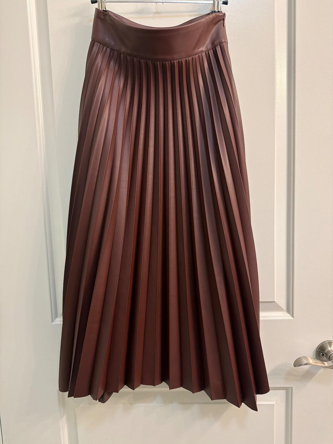 Brown pleated skirt hanging on a white door. The texture and sheen of the material stand out in the image.