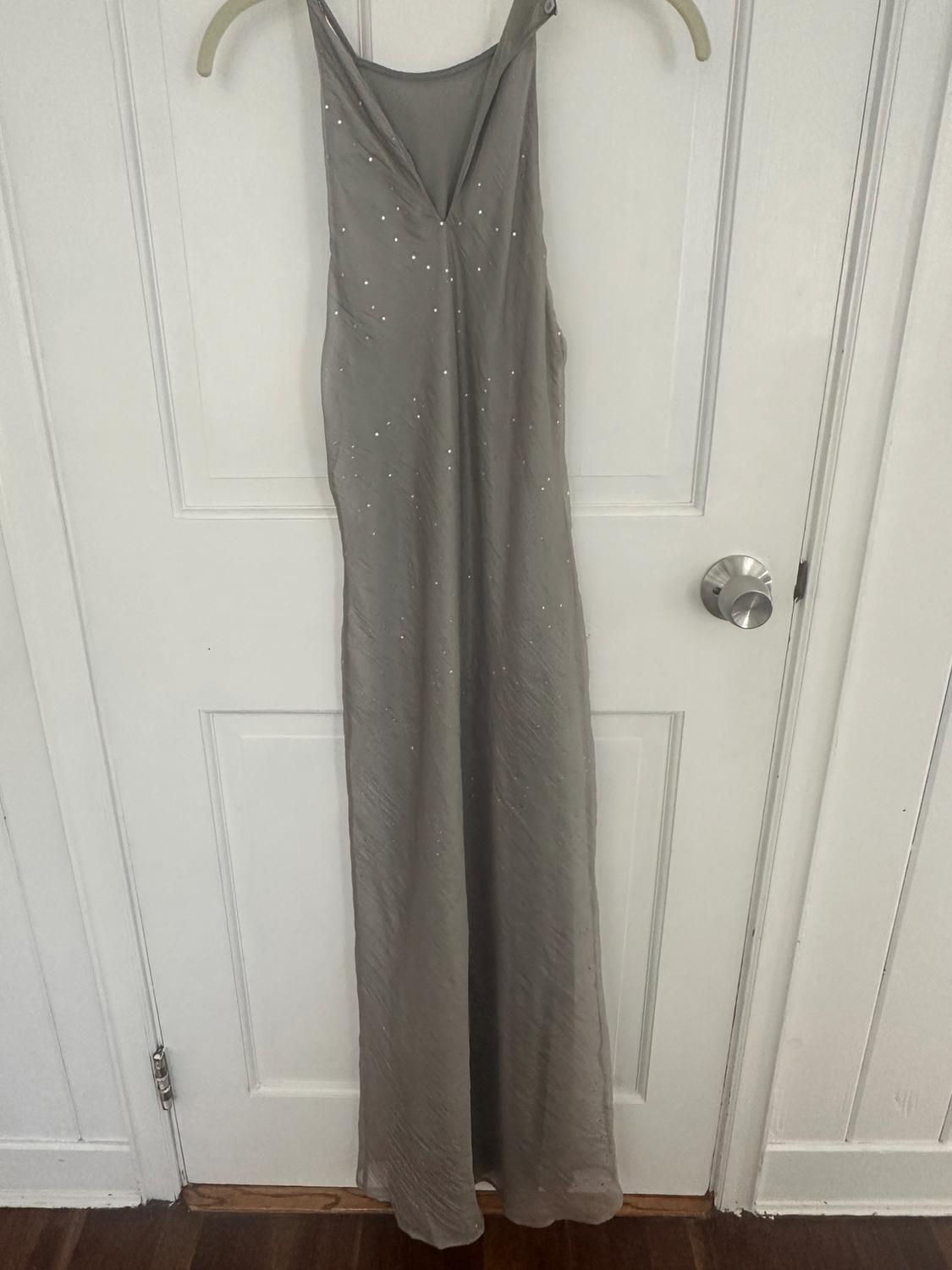 Long gray sleeveless dress with sparkly details, hanging on a hanger on a white wooden door.