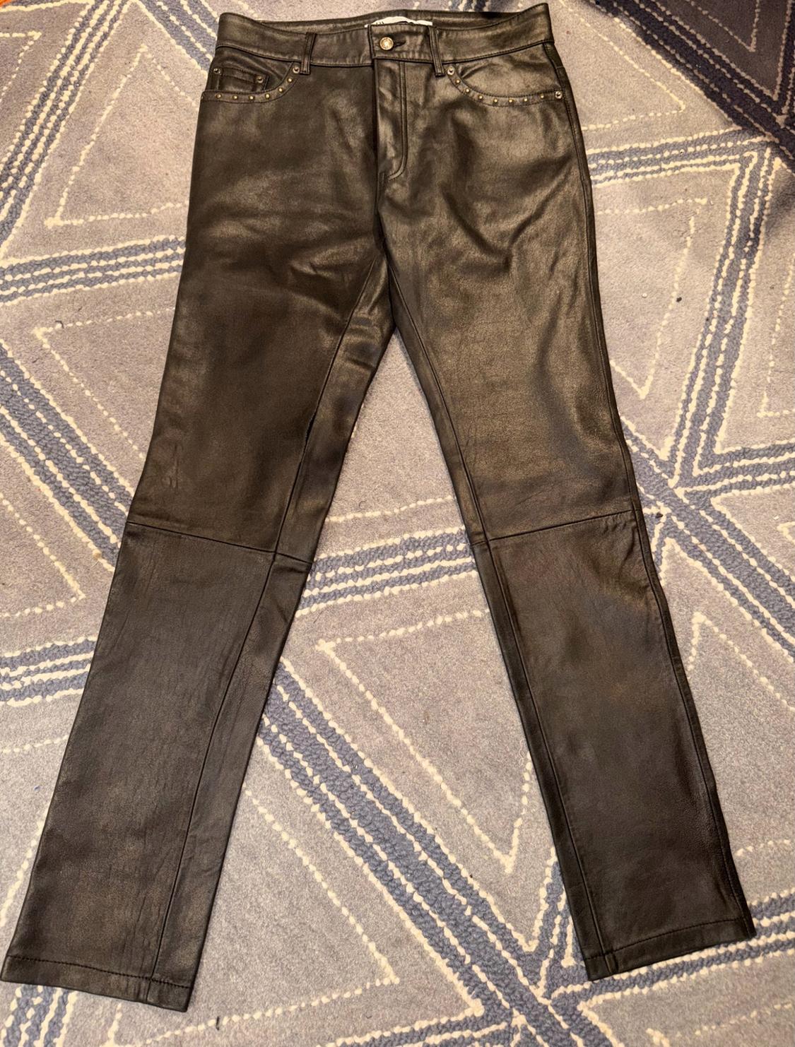 Black trousers with stitching on the knees and studs on the pockets, on a blue rug with a geometric pattern.