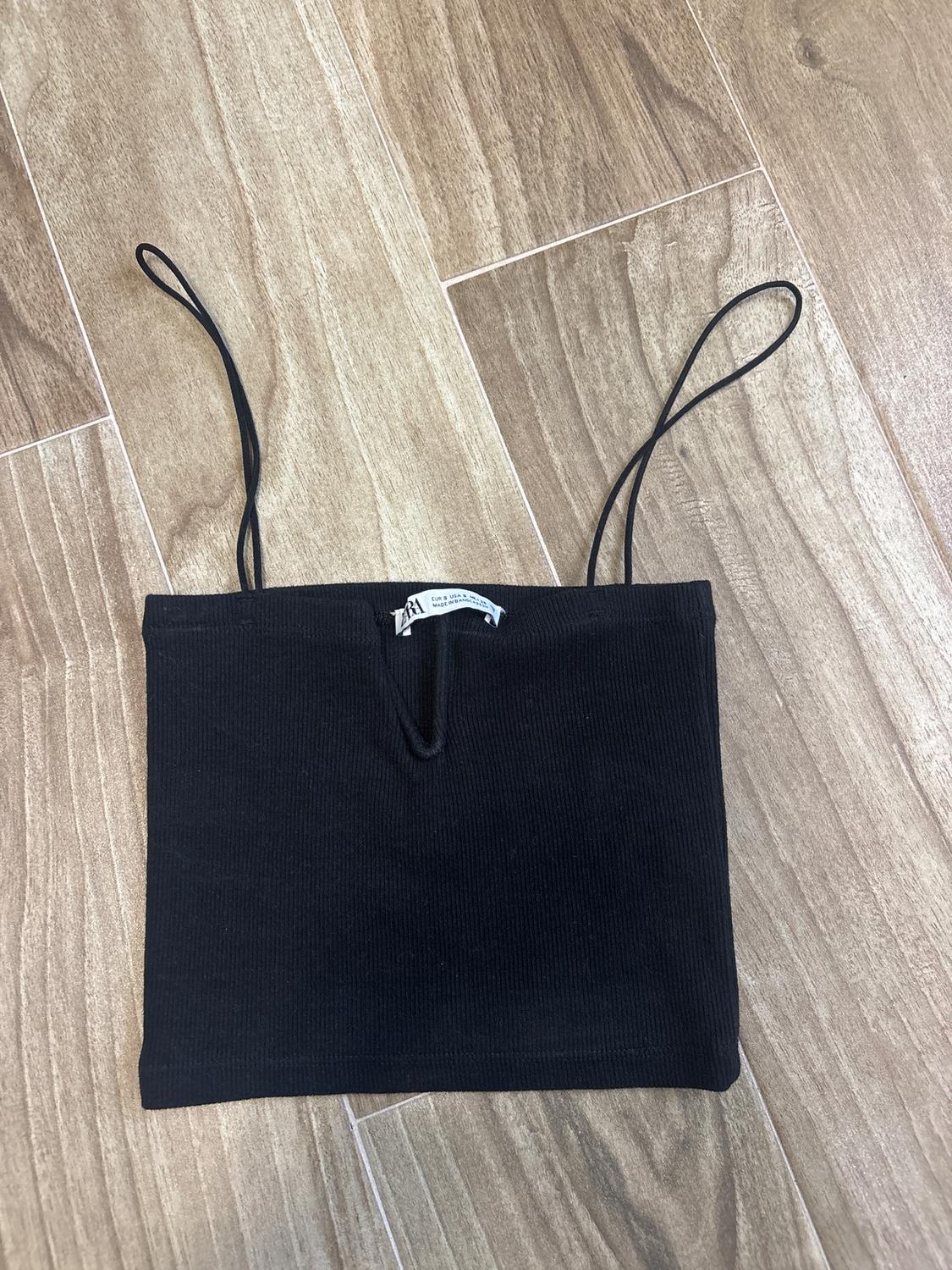 Black spaghetti-strap top on a light wooden floor. Visible tag in the center of the upper edge.