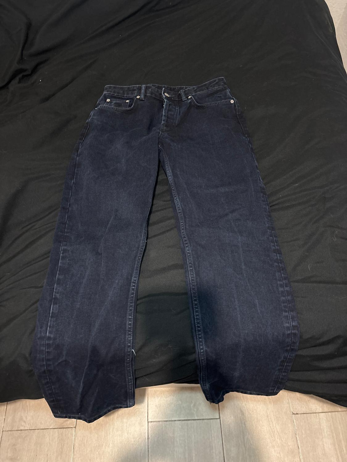 Dark blue jeans laid out on a bed with a black bedspread, showcasing a classic and relaxed style.