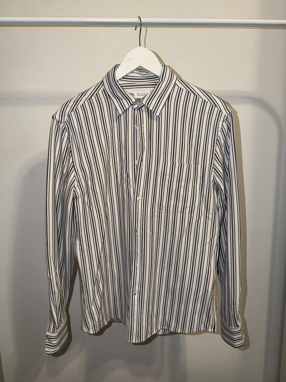 Black and white striped shirt hanging on a white hanger against a neutral background.