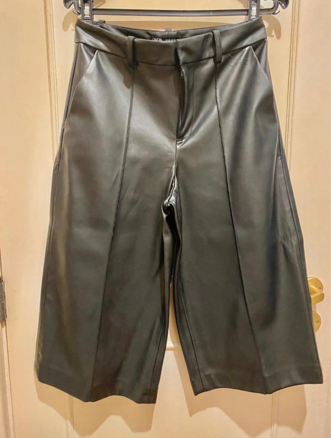 Black faux leather shorts hanging on a hanger over a light wooden door.