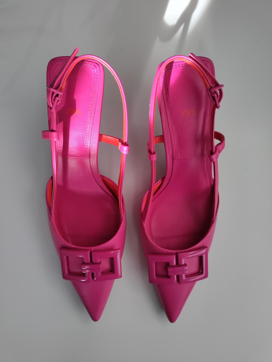 Bright pink high heels with pointed toes and square buckles, seen from above on an illuminated white background.