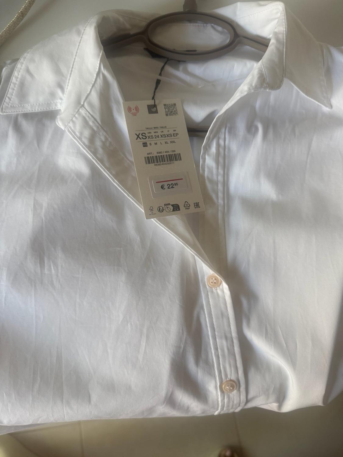 White button-up shirt on a hanger. Label: SIZE / SIZE / SIZE XS XS 24 XS XS EP ART.: 8382 / 404 / 250 08382404250017 €22.95.