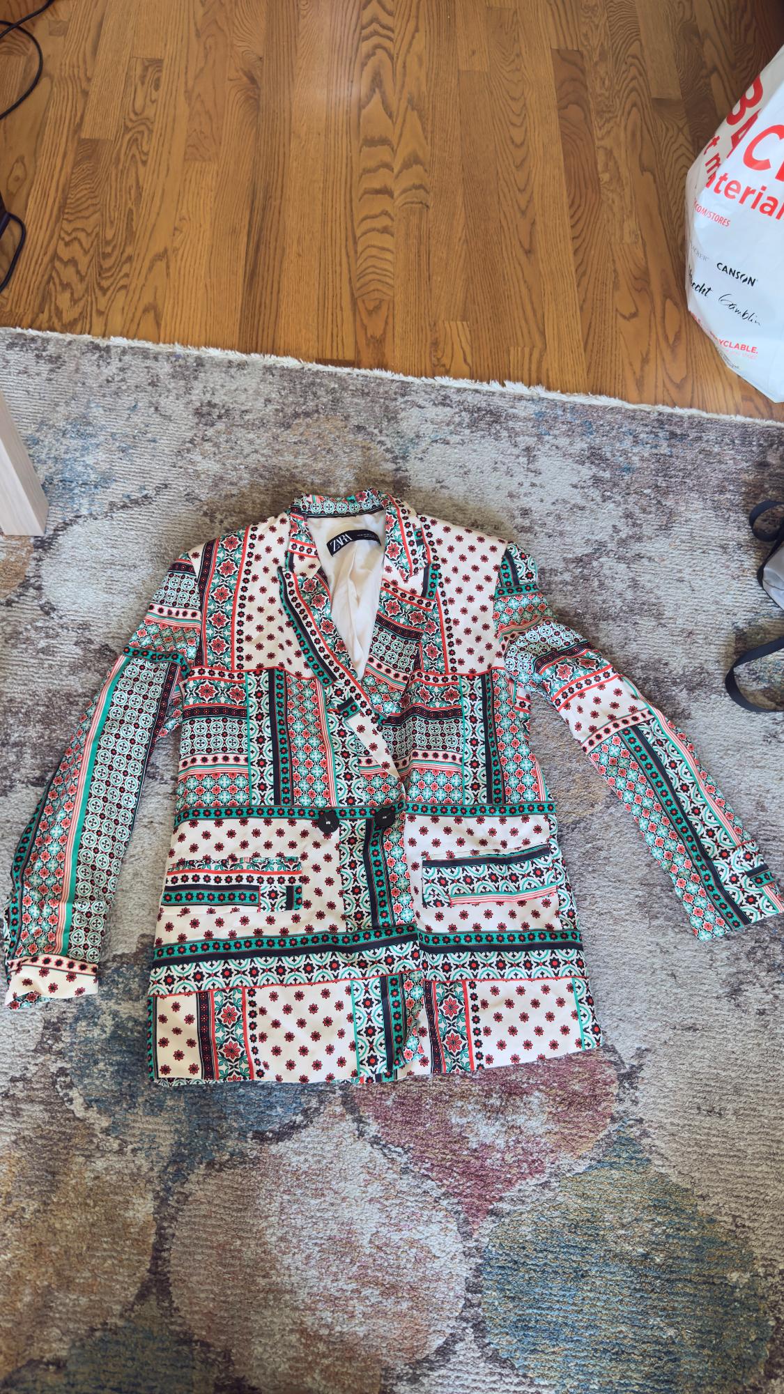 Multicolor patterned jacket with geometric patterns on textured carpet and wooden floor. Visible label inside.
