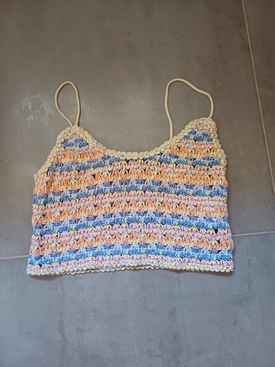 Crochet crop top with thin straps and horizontal stripes in pastel shades, on a grey tiled floor. Casual style.