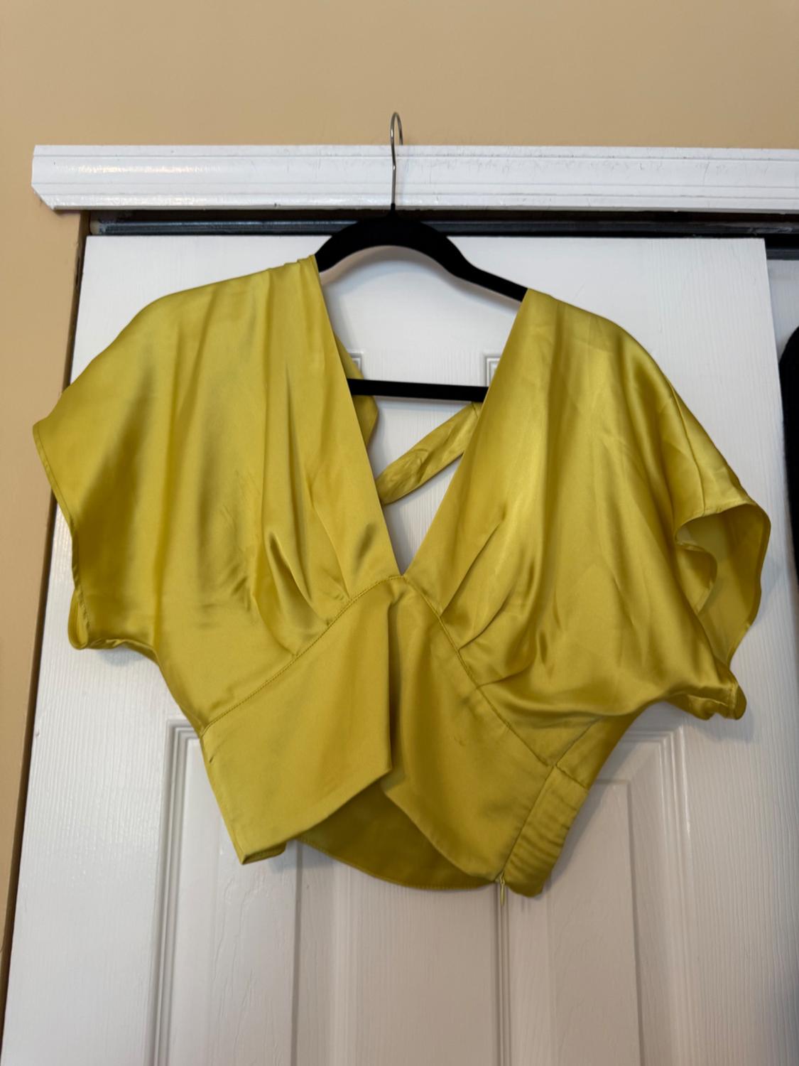 Yellow satin short-sleeved blouse hanging on a black hanger over a white door.