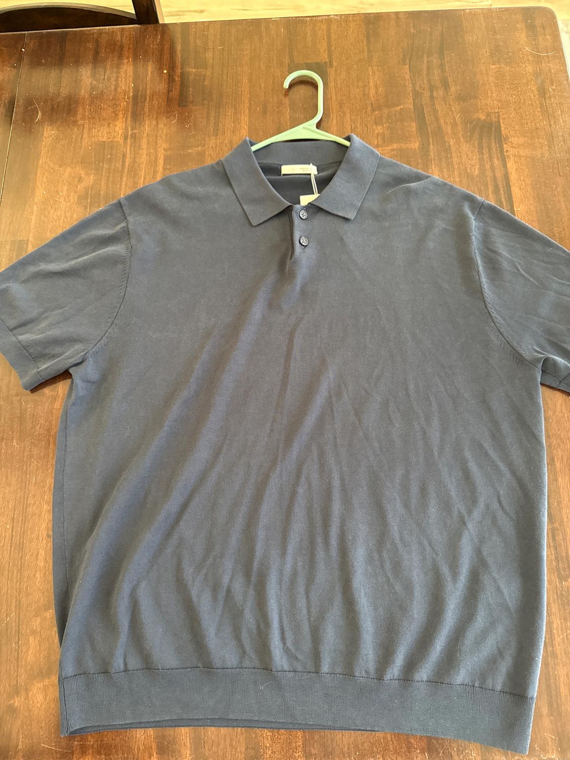 Dark blue polo-style shirt with a collar and short sleeves, hanging on a green hanger over a wooden table.