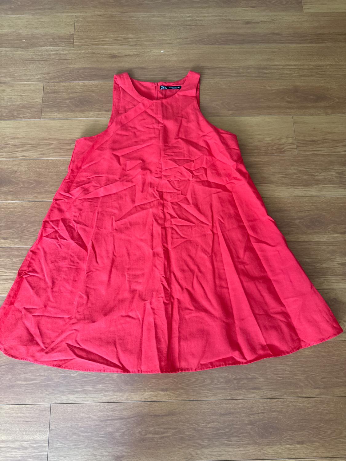 Red sleeveless dress on a wooden floor. Wrinkled fabric, loose fit and visible label on the neck.
