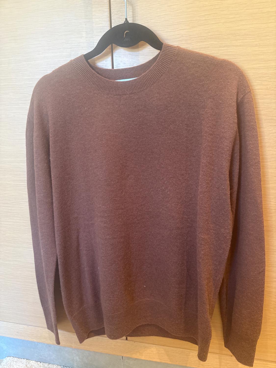 Fine-knit brown jumper hanging on a black hanger, against a light wooden background.