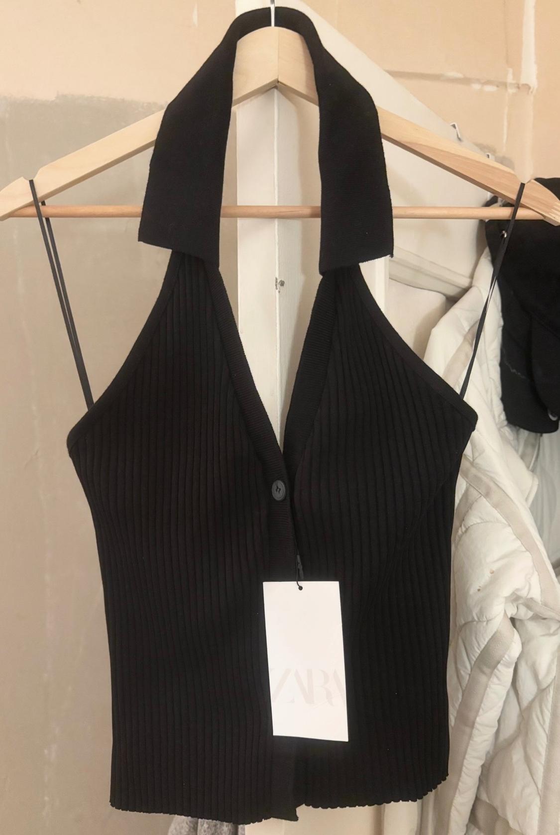 Top halter μαύρο rib με V λαιμόκοψη και μπροστινό κουμπί σε ξύλινη κρεμάστρα. Ετικέτα με το κείμενο Zara.