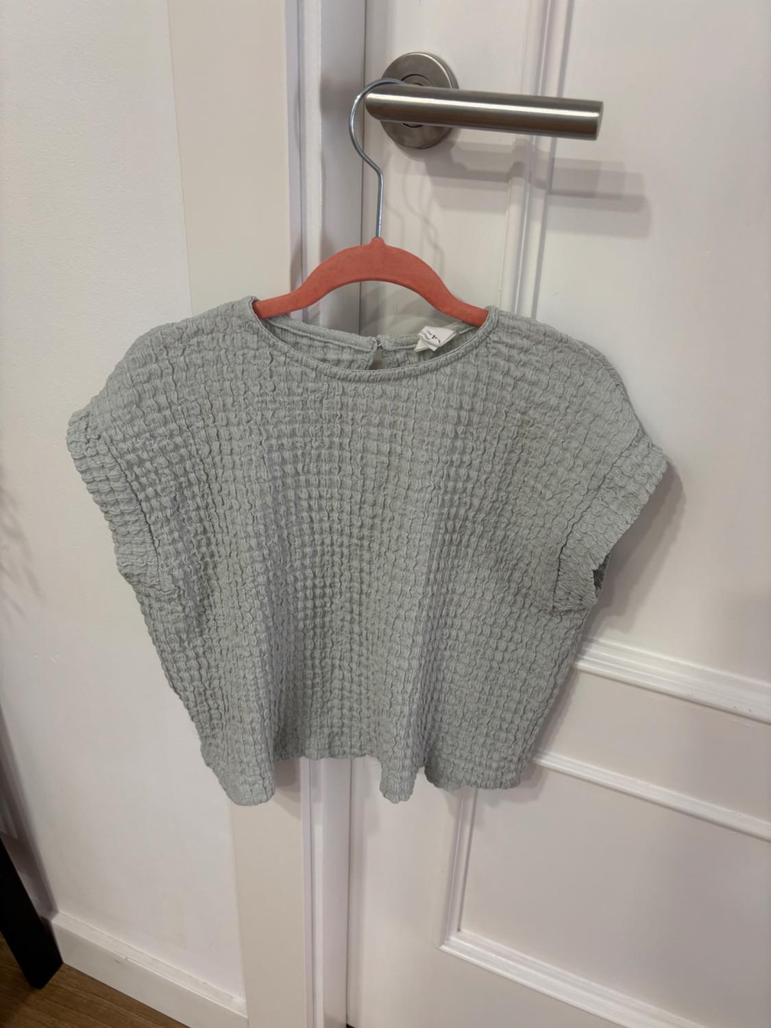 Textured grey blouse hanging on a red hanger over a white door with a metal handle.