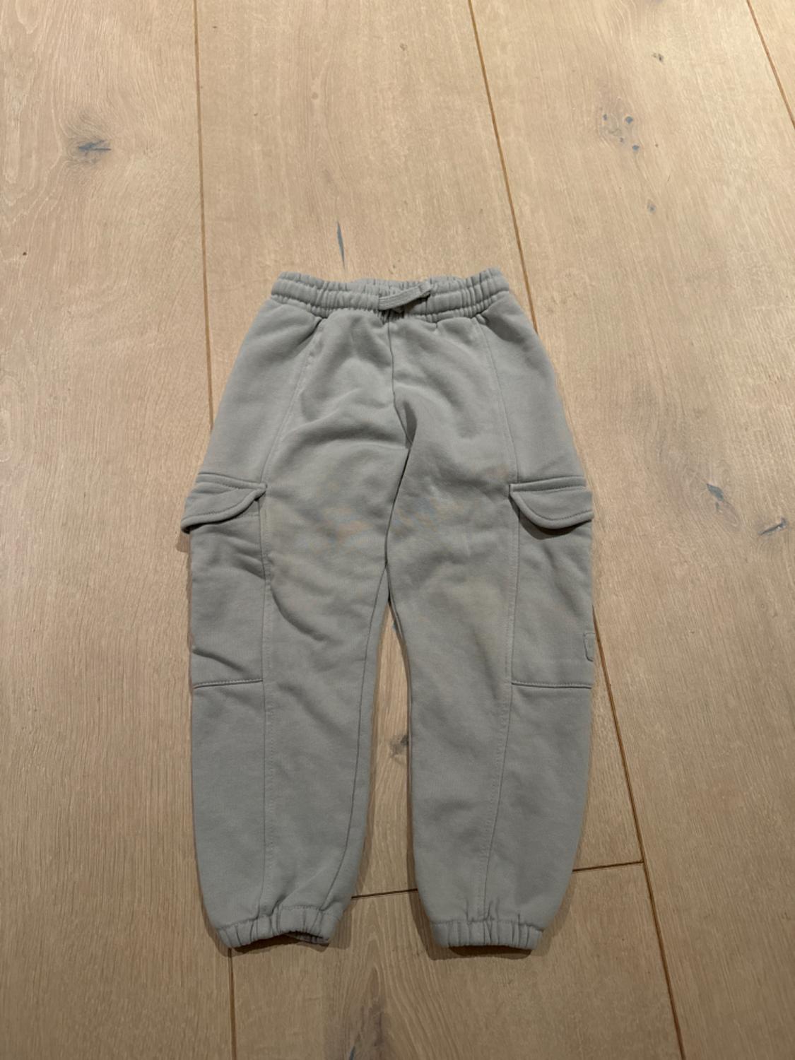 Grey kids' cargo trousers with an elasticated waist and side pockets, on a light wooden floor.