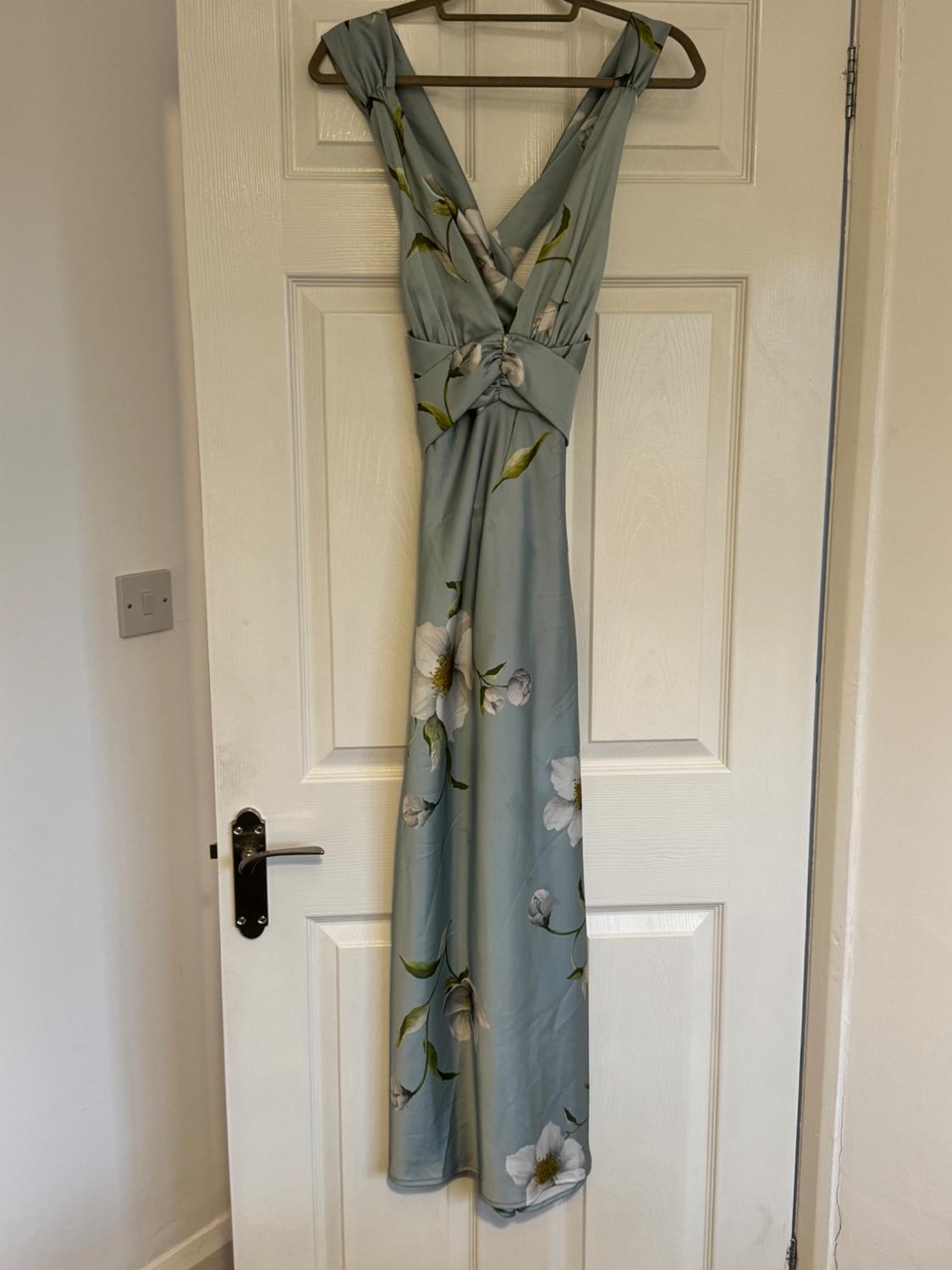 Light blue maxi dress with white and green floral print, hanging on a hanger over a white door with a metal doorknob.