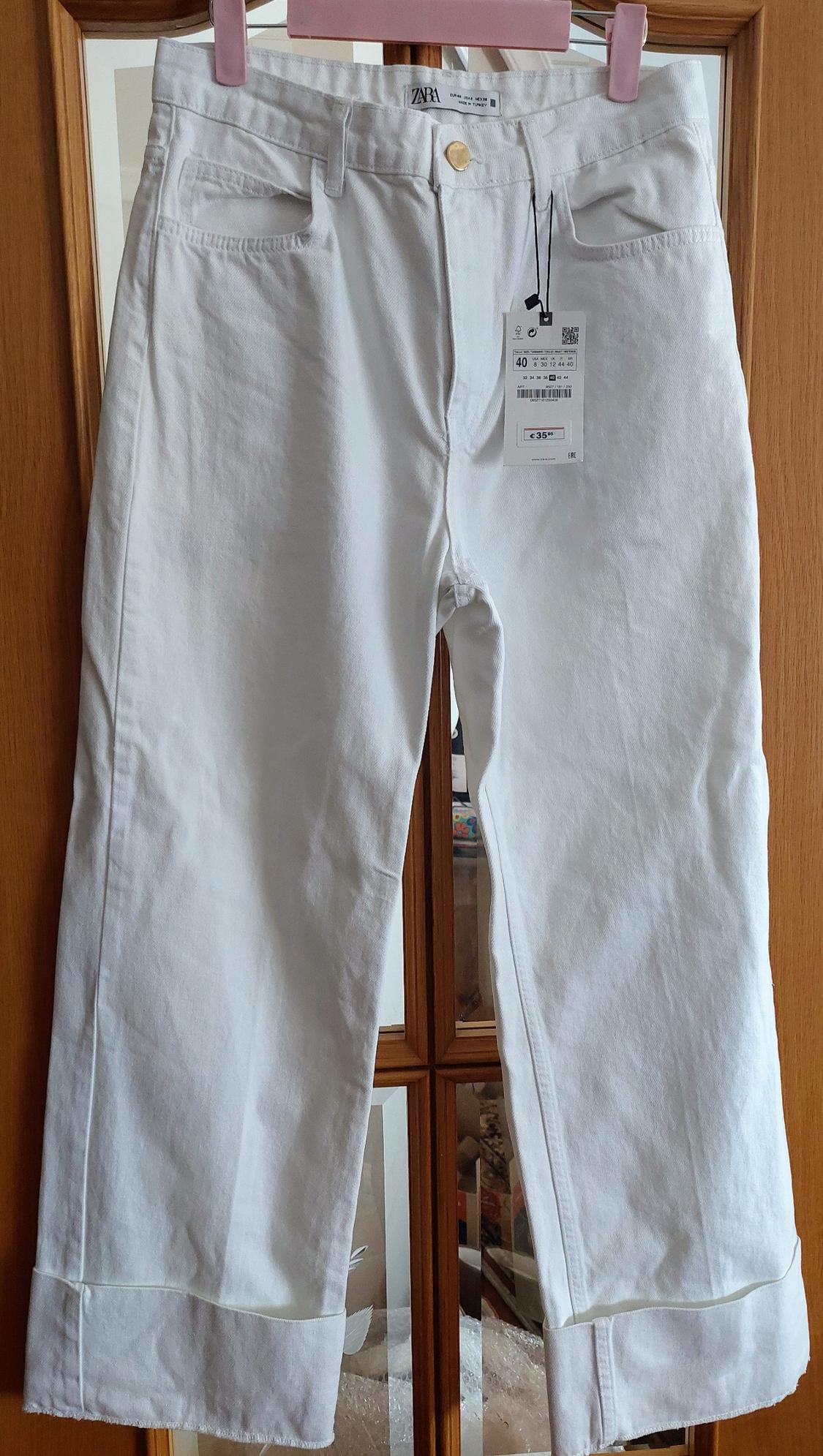 Front view of white trousers with front pockets and visible label.